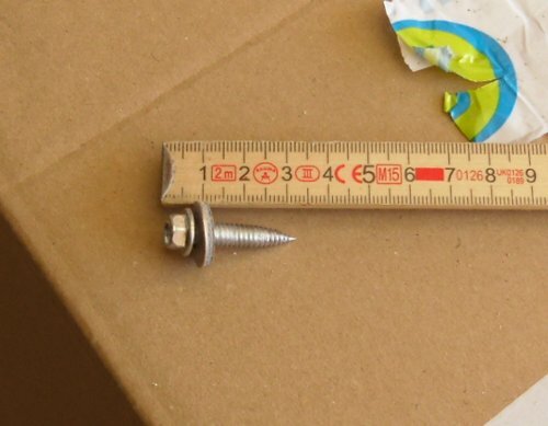 En mätsticka som visar 5 cm och en 6,0x25 mm tunnplåtskruv ligger på en brun yta.