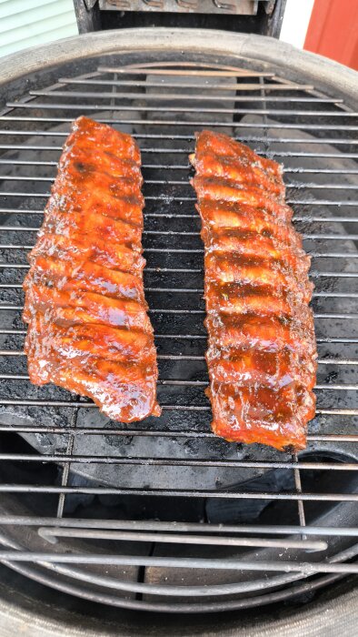 Två revbensspjäll täckta med barbecue-sås grillas på en kolgrill.
