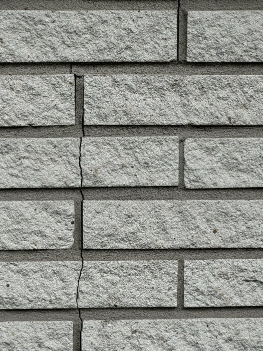 Spricka i murad yttervägg av gråa tegelstenar i ett radhus från 70-talet, sprickan går vertikalt genom några av stenarna.