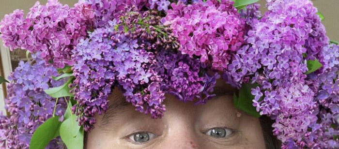 Person med en blomsterkrans gjord av lila och rosa syrener på huvudet.