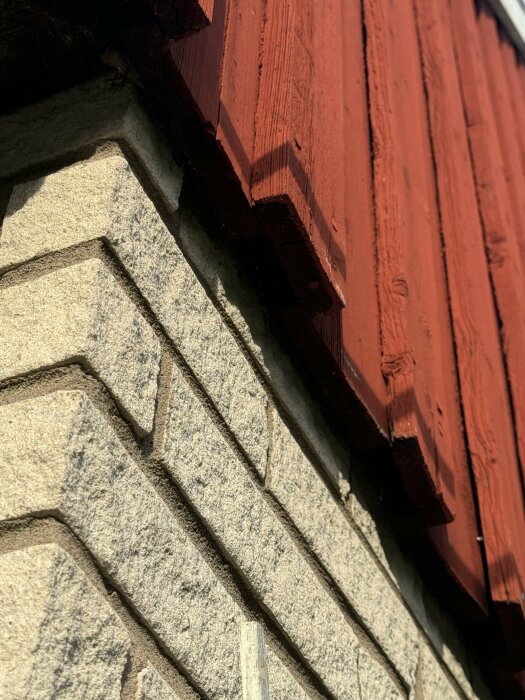 Närbild av en fasad med träpanel upptill målad i rött och tegel nedtill, visar övergången mellan dessa material.