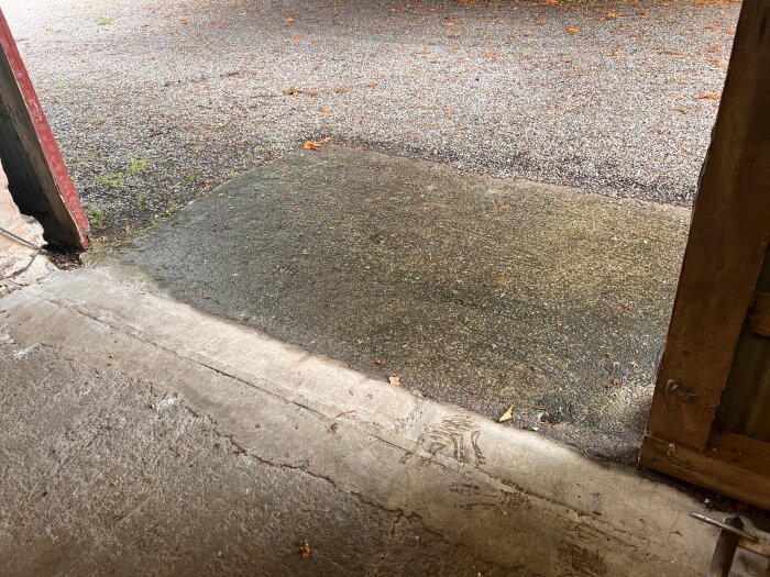 Bild utifrån en byggnad med en betongplatta framför en portöppning, där grus utanför plattan är något högre vilket orsakar vattenavrinning mot porten.