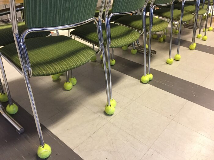 Gröna stolar med metallben i ett rum. Tennisbollar har satts fast på benen för att skydda golvet och minska ljud.