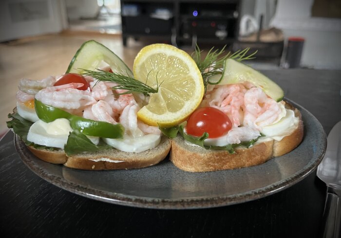 Två räkmackor på tallrik med räkor, sallad, tomat, citron, gurka och majonnäs på bröd.