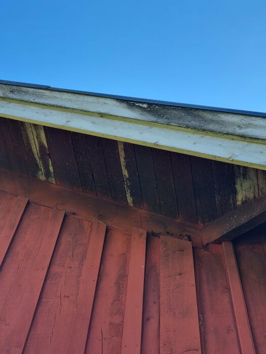 Närbild på husets tak och fasad, med synliga mögelfläckar och missfärgningar på under taket på en av husets sidor, fotograferad från marknivå.