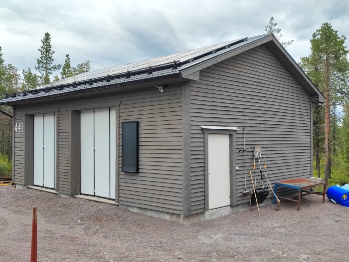 Garage målat med Auson Tjärvitrol, ljusbrunt och grått med dubbla vita dörrar och en sidodörr, beläget i skogsområde, tre år gammalt.