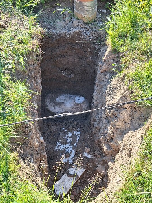 Utgrävd grop i marken som visar en del av en sluten tank med PVC-rör synligt ovan marken.