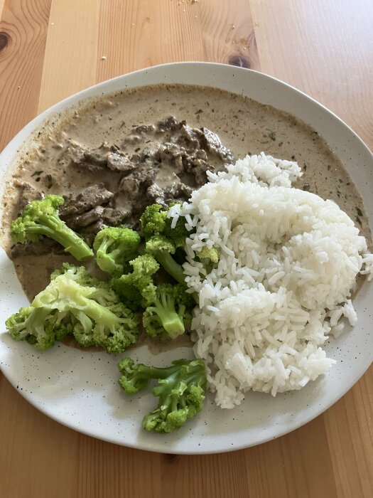 Överblick av en tallrik med lövbiffsgryta med dijonsenap och dragon, serverad med ris och broccolibuketter på ett träbord.
