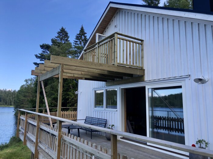 Nybyggt träräcke på vitmålad balkong och terrass på ett hus vid sjön en solig dag.