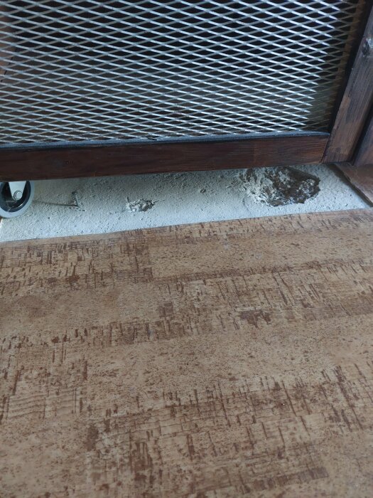 Bild av golvyta där en del av mattan saknas, vilket exponerar underliggande betong med skador efter att en garderobsfront har tagits bort under renoveringen.