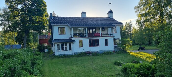 Vit tvåvånings Disponentvilla från 1935, med veranda på övervåningen, omgiven av träd och grönska i Sågmya, Dalarna.