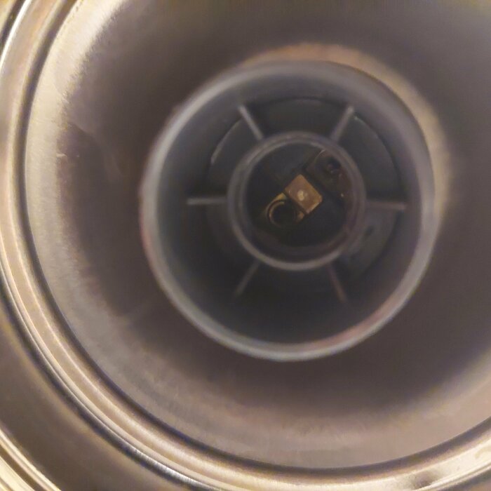 Närbild på insidan av en metallisk ventil eller rör med en komponent i mitten omgiven av plastdelar.