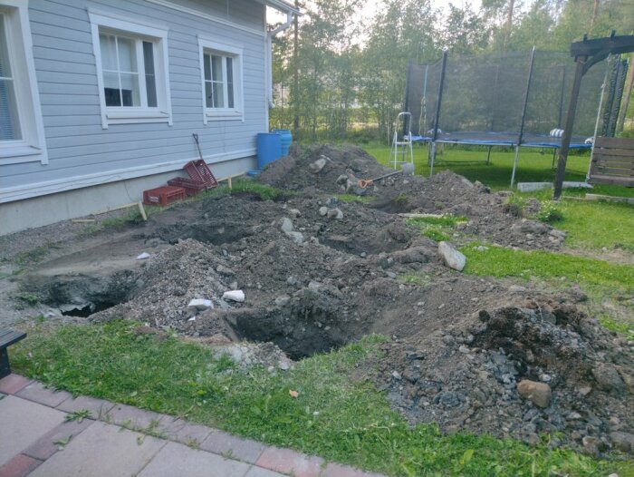 Grävt område intill ett hus med djupa hål i marken, jordhögar och verktyg; projekt handlar om att hitta en stark och smidig bygglösning.