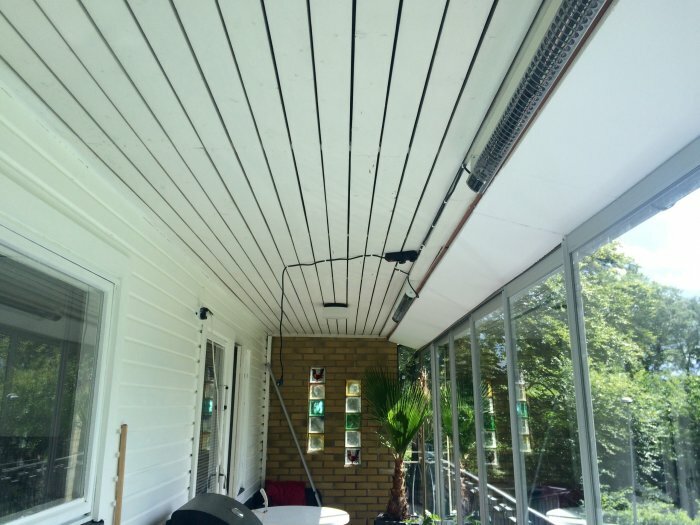 Undertak med grundmålad ytterpanel på en balkong, med mellanrum mellan plankorna och infällda spotlights, samt en uppvärmningslampa på sidan.