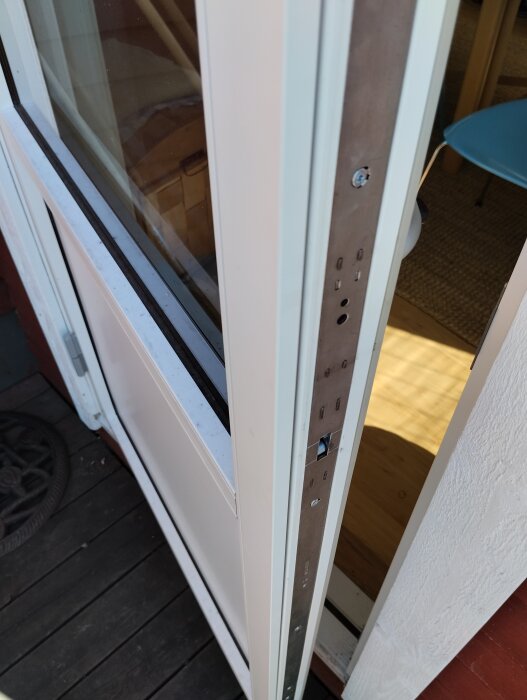 Altandörr med vit träkarm och aluminiumbeklädnad, sedd från insidan. Dörren saknar ytterhandtag. Skruvar och tätningslist synliga vid dörrkarmen.