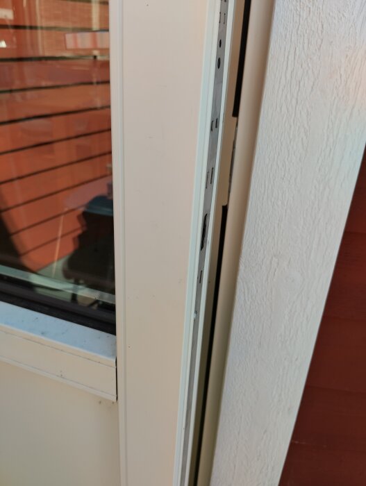 Altandörr med aluminiumbeklädnad visas från sidan, dörrbladet kan inte öppnas utifrån. Närbild på lätt öppnat dörrfäste och tätning mellan dörren och väggen.