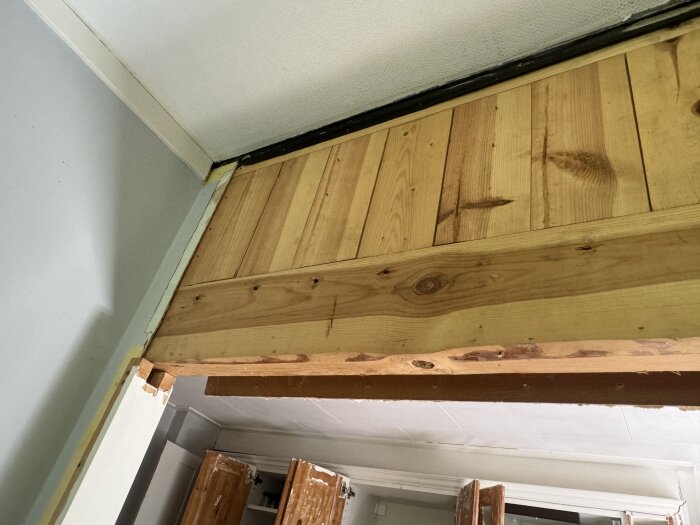 Bild visar en närbild av en nybyggd träram ovanför en dörröppning i ett hus med omålade träpaneler.
