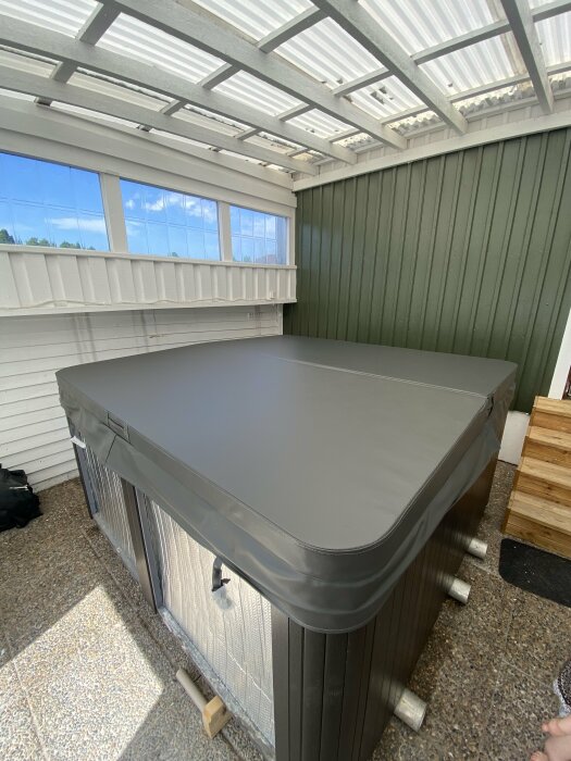 Nytt spatäcke över en jacuzzi på en täckt uteplats med vit pergola och grön fasad i bakgrunden.