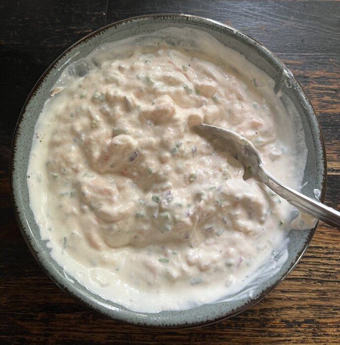 Skål med en röra av varmrökt lax, räkor, gräddfil, gräslök, rödlök, citronsaft, peppar, kaviar och majonnäs med en sked i.