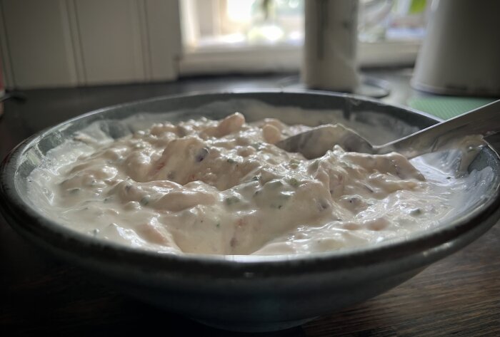 Närbild på en skål med hemgjord lax- och räkröra, serverad med gräddfil, gräslök och rödlök, för lunchen. En sked ligger i röran.