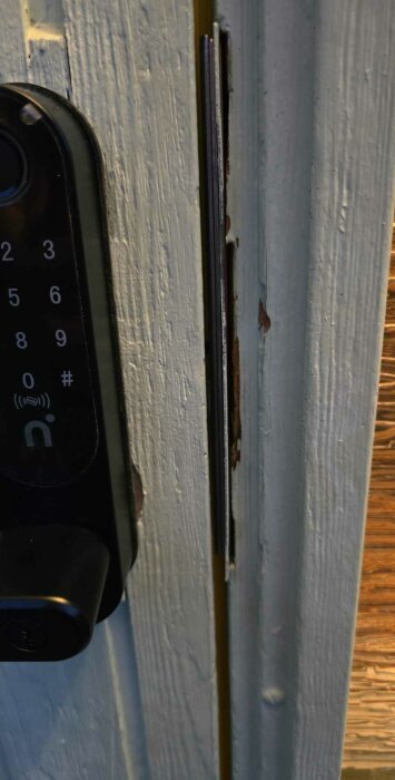 En närbild av en dörrkarm med en elektronisk dörrlås och ett metalliskt slutbleck monterat i karmens urgröpning.