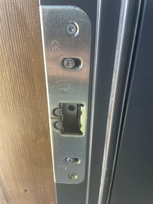 Närbild på en dörrkarm med en metallplatta och skruvar vid låset, med träpanel till vänster och metall till höger.