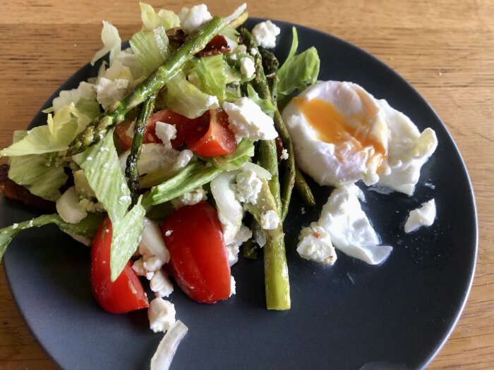 En tallrik med sallad innehållande sparris, tomater och fetaost samt ett ägg med rinnande gula.