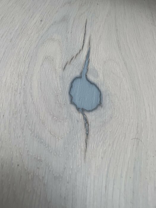 Närbild på ett ljust trägolv med en kvist som har fått en blåaktig färg.