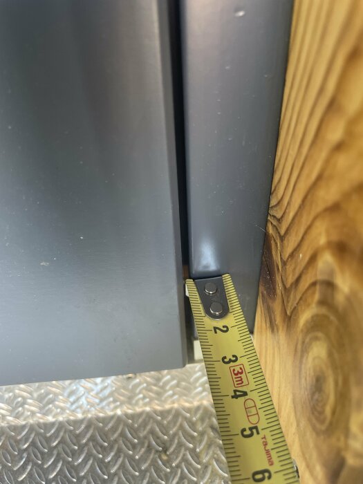 Ett måttband visar avståndet mellan en stängd dörr och en karm av stål och trä.