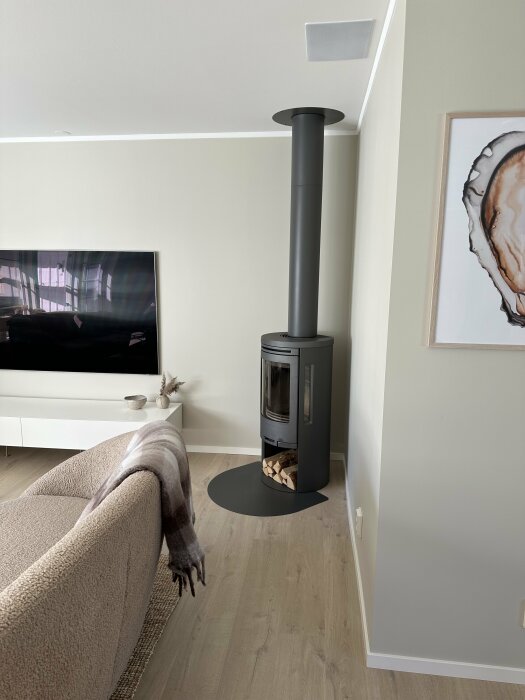 Nyinstallerad svart kamin med ved förvarad under, belägen vid väggen bredvid en beige soffa med en filt och en TV på en vit mediabänk i vardagsrummet.
