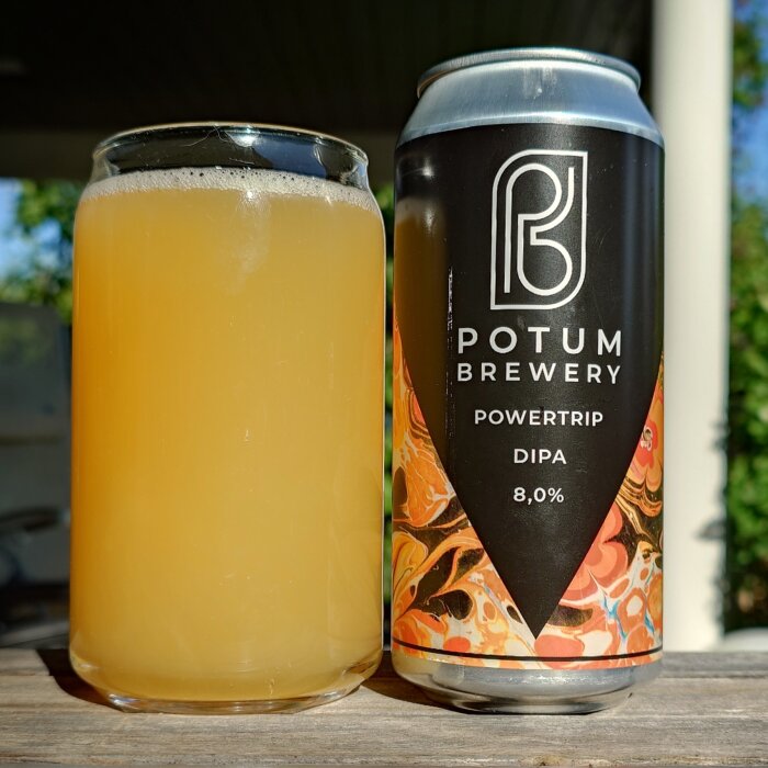 En burk med Potum Brewery Powertrip DIPA, 8,0% alkohol, och ett glas med gul öl som står på ett träbord utomhus.