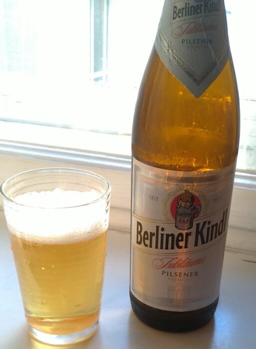 Flaska med Berliner Kindl pilsner och ett fyllt glas öl på ett fönsterbräde i Berlin.