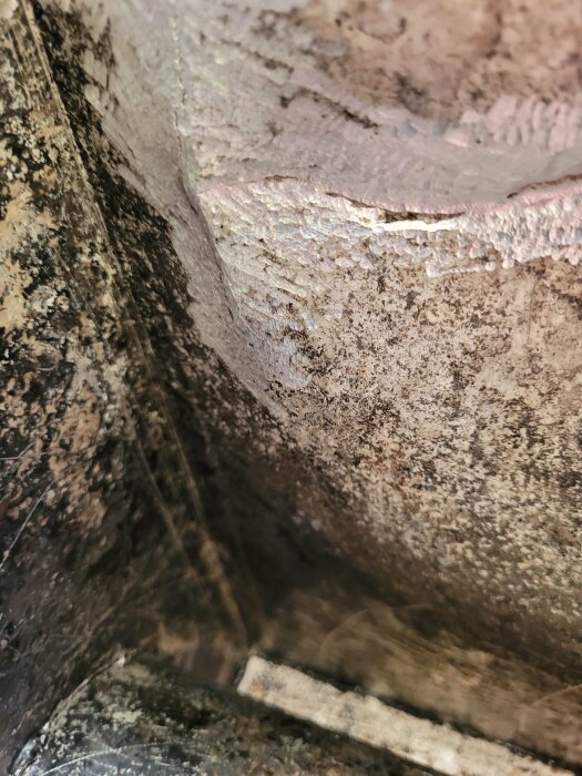 Närbild på en sprucken aluminiumkant i en kamin till en badtunna, kantens yta är ojämn med tydliga skador och rost.