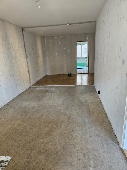 Rum under renovering med synliga väggar och golv; gammalt golv har tagits bort för att undersöka underlaget. Ett stort fönster med ljusinsläpp syns i bakgrunden.