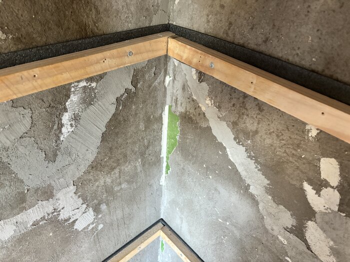 Trävinklar med syllisolering monterade på betongvägg i ett rum under renovering. Isoleringen placeras mellan trä och vägg för att förhindra fuktproblem.