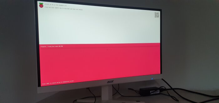 Bildskärm med en uppstartsskärm för Raspberry Pi med röd och vit bakgrund. Text på skärmen visar installationsstatus och bootlägen.