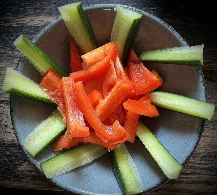 En skål med gurk- och paprikastavar på ett bord.