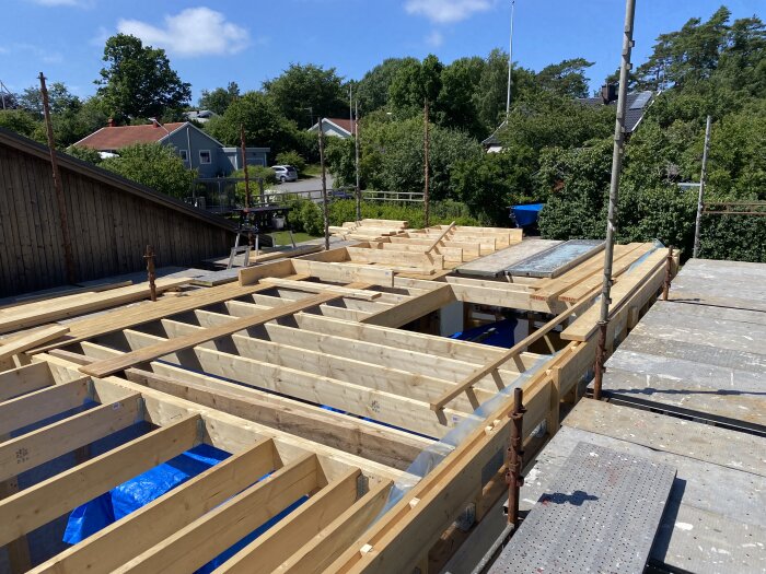 Träkonstruktion för nytt bjälklag uppreglat på ett byggprojekt, med träbjälkar och byggnadsställningar i en bostadsmiljö.