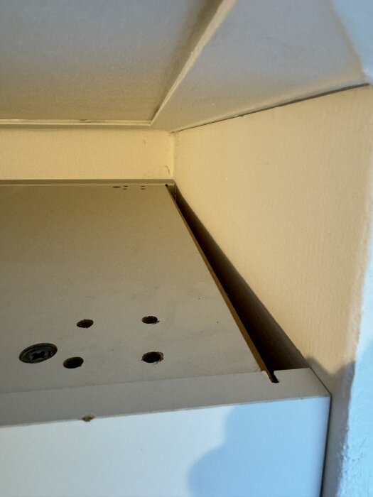 Garderoeb i et rum viser den øvre del af garderoeben med ventilationshuller og en luftspalte bagved.