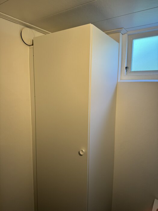 Garderob i källare med luftspalt mellan väggen och garderoben, samt ett fönster ovanför garderoben.