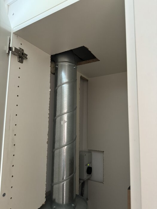 Ventilationsrör och elektrisk installation synliga inuti en garderob med utskurna hål i vägg och tak.