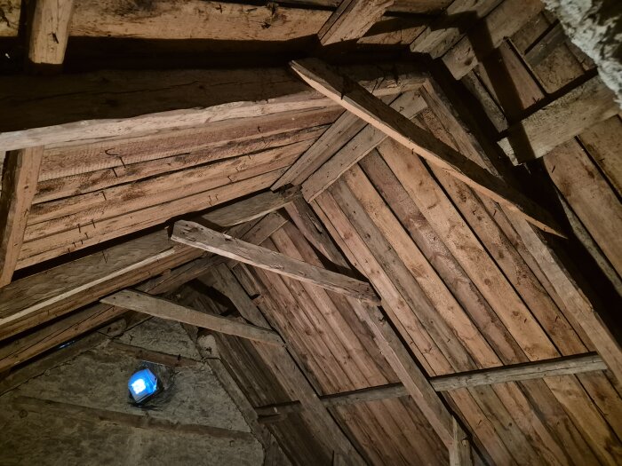 Vindsbjälklaget sett underifrån med träbjälkar placerade med cirka 145 cm mellanrum. Ett litet fönster syns högst upp i bilden.