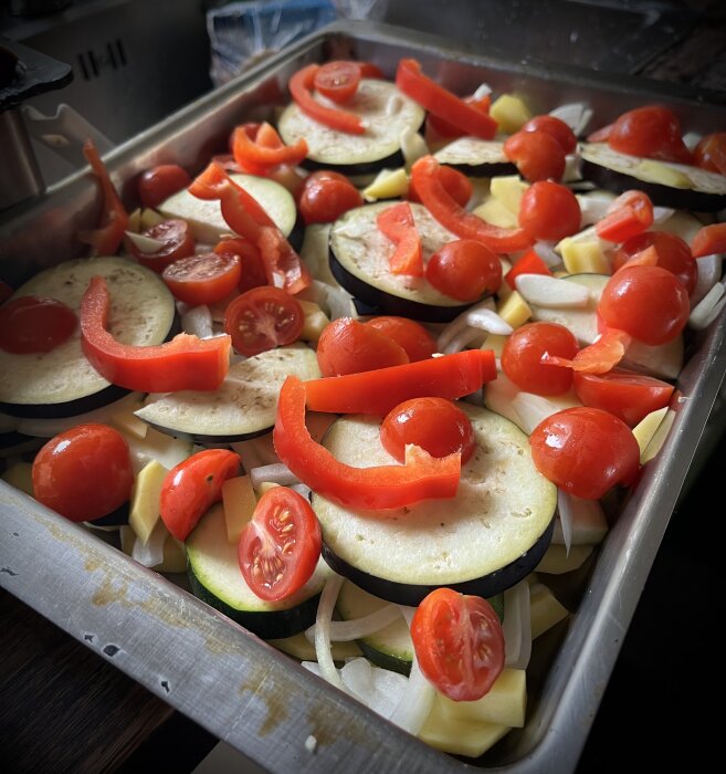 Gratäng med tomater, röd paprika, aubergine, squash, lök och potatis i en ugnsform, redo för tillagning.