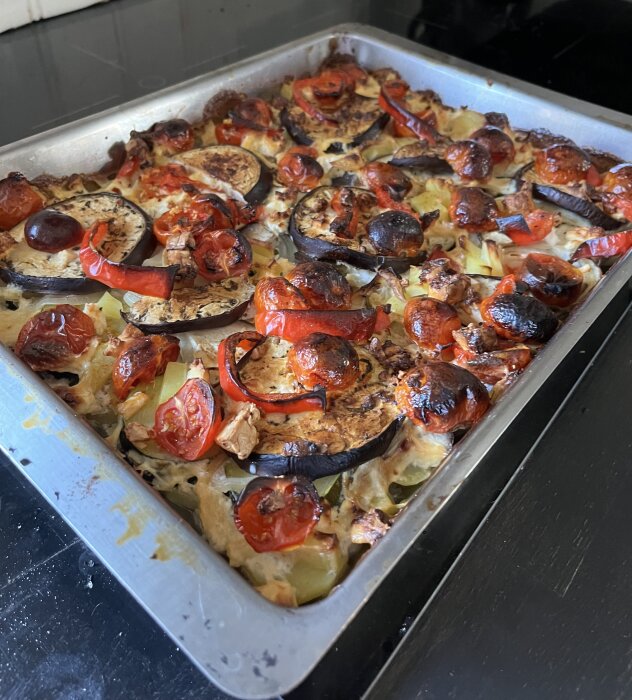 Gratäng med potatis, squash, aubergine, paprika, tomater och fetaost i en ugnsform, med lite brända tomater på toppen och krämig sås.