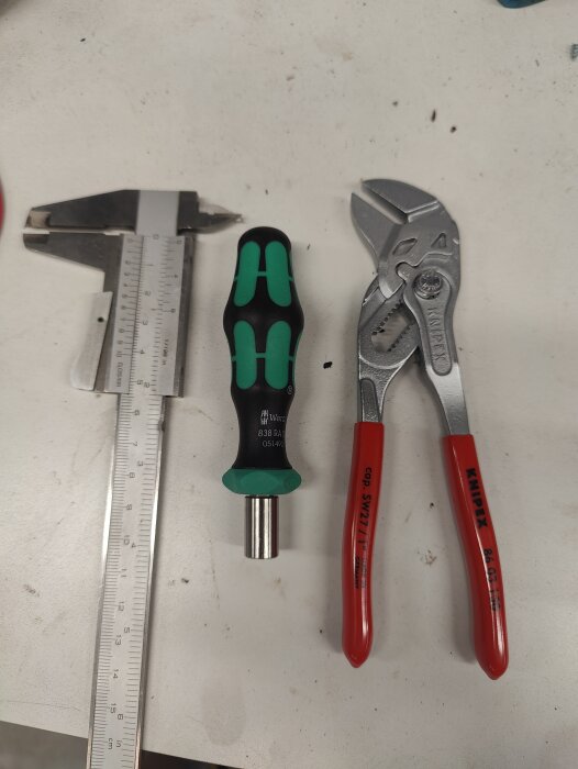 En skjutmått, en liten Wera-skruvmejsel och en Knipex-parallelltång ligger på en vit yta.