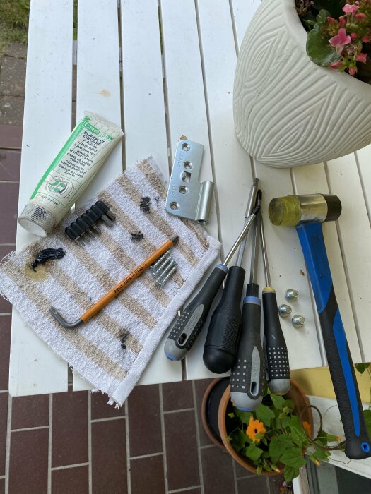 Gör-det-själv projekt för smörjning av dörrgångjärn: bild på verktyg, smörjmedel, skruvmejslar, insexnyckel, gångjärnet ASSA Abloy 3248 och en duk på en vit bordsbräda.