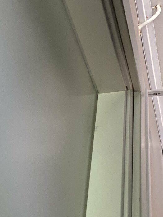 Tätningslist i övre hörnan av en dörrkarm, med en mindre springa synlig ovanför dörrhandtaget och kabel på sidan.