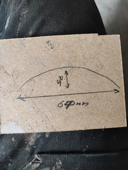 Handritad skiss på träbit som visar mått för rundat glasdörr, 64 cm bredd och ca 7,5 cm djup, på en mörkfärgad bakgrund.