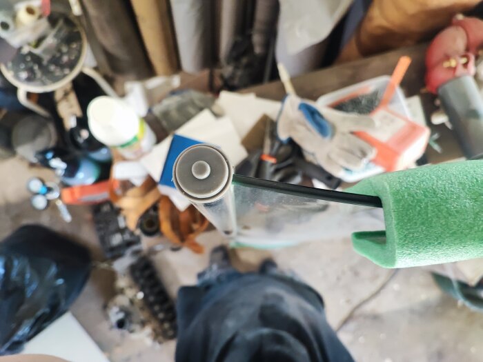 Närbild på ovankant av en rundad duschdörr med grön skyddande skumplast, diverse verktyg och material i bakgrunden på ett verkstadsgolv.