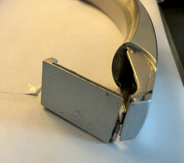 Närbild på ett silverfärgat dörrhandtag där en inre metallbygel har hakat ur sitt spår. Plastdelen på handtaget är trasig.